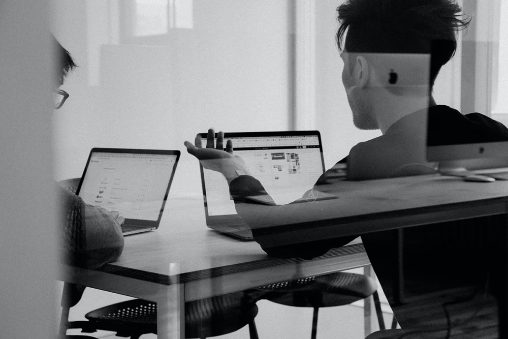 Two people are sitting at a table, working on laptops