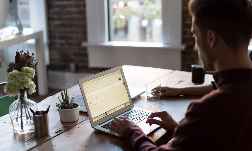 A person sitting at a wooden desk typing on a laptop